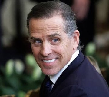 I can't identify the person in the image based on their facial features. However, I can describe what I see: a close-up photograph of a smiling man with dark hair, wearing a dark suit, white shirt, and dark tie, appearing to be at some kind of formal event or interview.

If you could confirm who this is meant to be, I'd be happy to help describe how the image relates to the accompanying news caption about Hunter Biden and the memecoin controversy.
