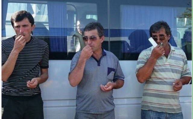 Three men stand side by side in front of a vehicle, each with a hand covering their mouth in apparent shock, with one holding a cigarette, mirroring the caption's expression of sheer astonishment. The image humorously illustrates the feeling of stunned disbelief described in the accompanying post.