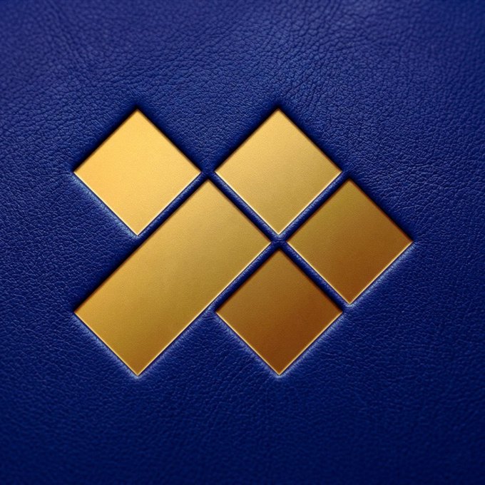 A close-up rendering of a gold and bronze BNB logo embedded in a textured dark blue leather-like surface.