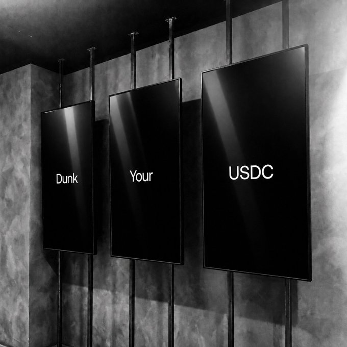 Three black display panels suspended by metal rods read "Dunk," "Your," and "USDC" against a textured gray wall, visually completing the phrase "Did you Dunk Your USDC?" from the accompanying post.