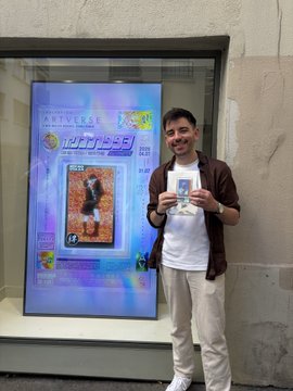 A man in a brown jacket stands proudly holding a phone displaying an image, posing in front of a digital advertising screen at the Musée d'Orsay that reads "IMPRESSION" and "CLAIR OBSCUR," connecting to the post's mention of the Renoir exposition and Clair Obscur Expedition 33 crossover.