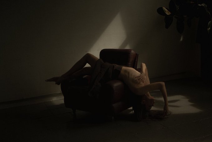 The image depicts a person in a contorted pose on a leather chair, illuminated by a shaft of light, representing the "Tango with demons" concept of embracing inner struggles as shared in the @6529Collections submission.