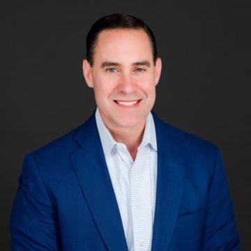 Frank Cappelleri, founder of CappThesis, is pictured in a professional headshot wearing a blue blazer over a checkered shirt, smiling against a dark gray background. His confident, polished appearance aligns with his bullish commentary on Bitcoin's potential breakout, lending credibility to his market outlook.