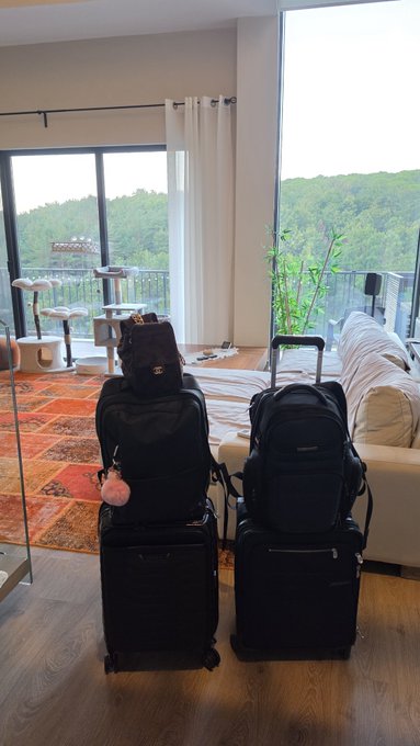 Two black rolling suitcases and matching backpacks (including one marked "Spectrolite") stand packed in a bright, modern living room, ready for a trip. The image ties to the post by capturing the traveler's departure for Canada, while the visible luggage symbolizes the pause in their trading and Bitcoin/DCA strategy amid the market downturn.