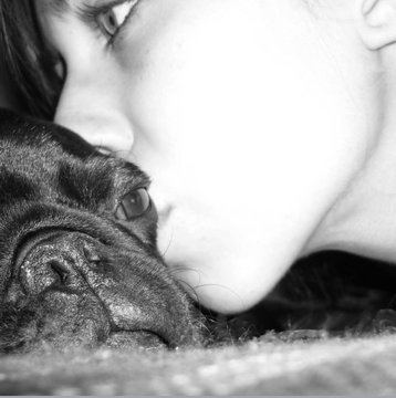 A black and white close-up photograph of a person's face pressed affectionately against a French bulldog.