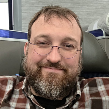A smiling man with glasses and a beard, likely Charles Hoskinson, is shown sitting in what appears to be a vehicle interior. The image pairs with a quote about Cardano's founder expressing frustration with discussing Ethereum.