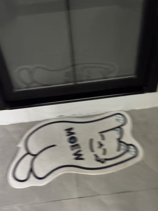 A small white fabric item with a cartoon cat outline and the word 'MEOW' sits on a windowsill in front of a dark window.