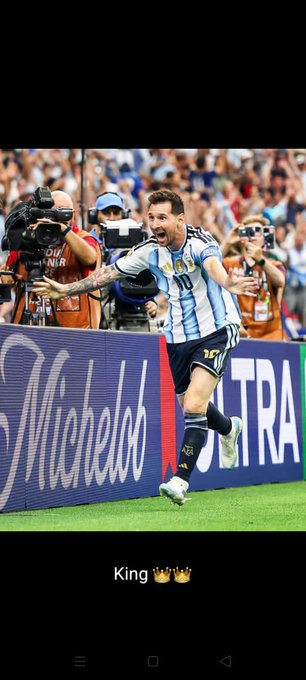 Lionel Messi, wearing Argentina's number 10 jersey, celebrates with arms outstretched in front of photographers near a Michelob Ultra advertising board, while the caption "King" with crown emojis crowns him as royalty of football.