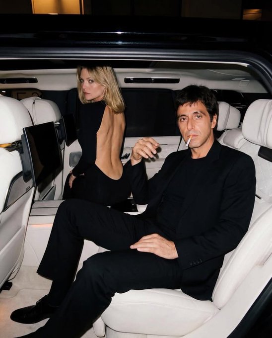 The image shows a man sitting in the back of a car, smoking a cigarette while wearing a black suit. A woman is also present in the scene, sitting next to him. The background features a car interior with white seats and a window on the side. There are two additional people visible in the image - one person standing behind the couple and another person standing near the car's rearview mirror.

The post includes text that reads "Swapped all my monad for $neet fuck it we ball". This phrase is likely a reference to a popular meme or joke, which suggests that the man smoking the cigarette might be associated with a certain subculture or lifestyle.