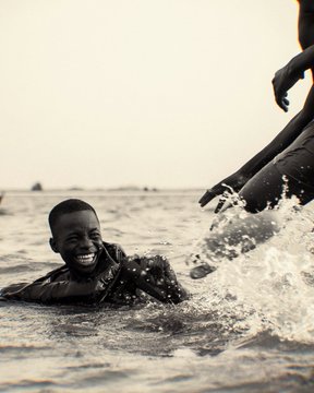 A sepia-toned photo of a young boy laughing joyfully while playing in ocean waves alongside another person.