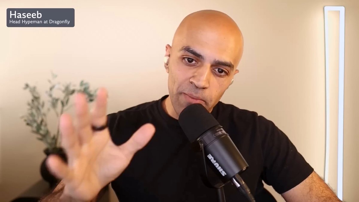 The image features a bald man wearing a black shirt, sitting behind a microphone with his hand raised. The caption reads "Haseeb asked Jeff if he ever envies centralized exchange founders One year later everyone envies Jeff and Hyperliquid". This suggests that the image is related to a podcast or interview where the host and guest are discussing the topic of centralized exchanges and their impact on the cryptocurrency market.

The man's baldness, black shirt, and microphone setup create an atmosphere for a serious discussion about the subject matter. The caption provides context by referencing a popular quote from Jeff Bezos, which adds depth to the image and reinforces its connection to the podcast or interview.