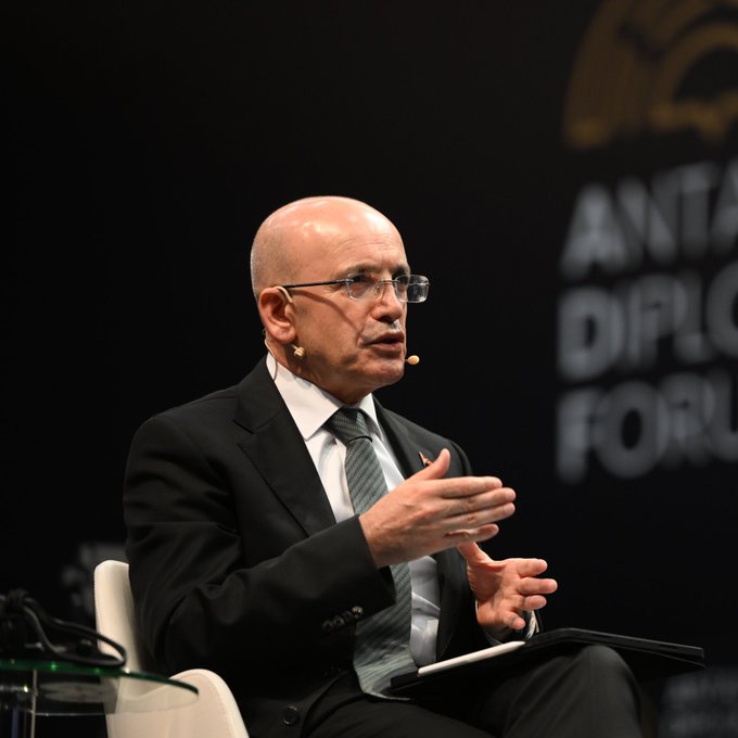 A bald man in a dark suit and glasses speaks while gesturing with his hands at what appears to be the Antalya Diplomacy Forum.
