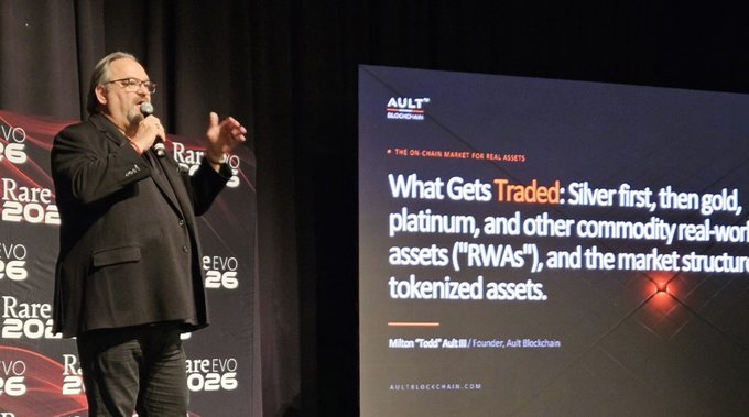 A man in a suit speaks into a microphone at the Rare Evo 2026 conference, presenting alongside a slide titled 'What Gets Traded' that discusses silver, gold, platinum, and other commodity real-world assets (RWAs) and tokenized assets.
