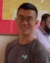 A smiling man wearing glasses and a gray shirt with a small logo stands indoors against a colorful pink and yellow background, embodying the post's narrative of crypto success and a dream lifestyle achieved through building viral projects, airdrops, and Web3 influence.