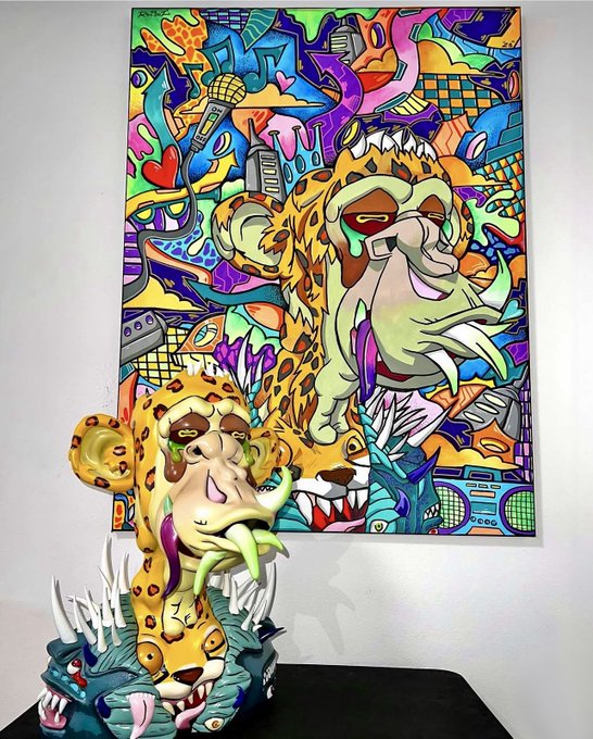 A vibrant, graffiti-style artwork featuring a leopard or jaguar is displayed as a flat painting on the wall, with a 3D sculpted version of the same animal placed in front of it on a black surface.