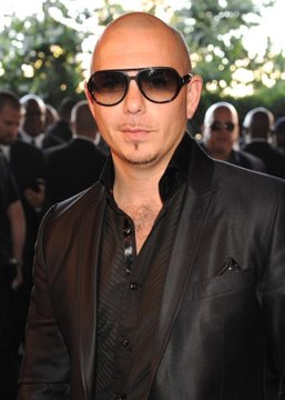 A bald man with sunglasses and a black satin blazer poses at what appears to be a public event, aligning with the post announcing Pitbull's launch of a new cryptocurrency called "Pitcoin." The image connects to the news by featuring the rapper/entrepreneur at the center of the announcement, though no "Pitcoin" branding or text is visible in the photo itself.