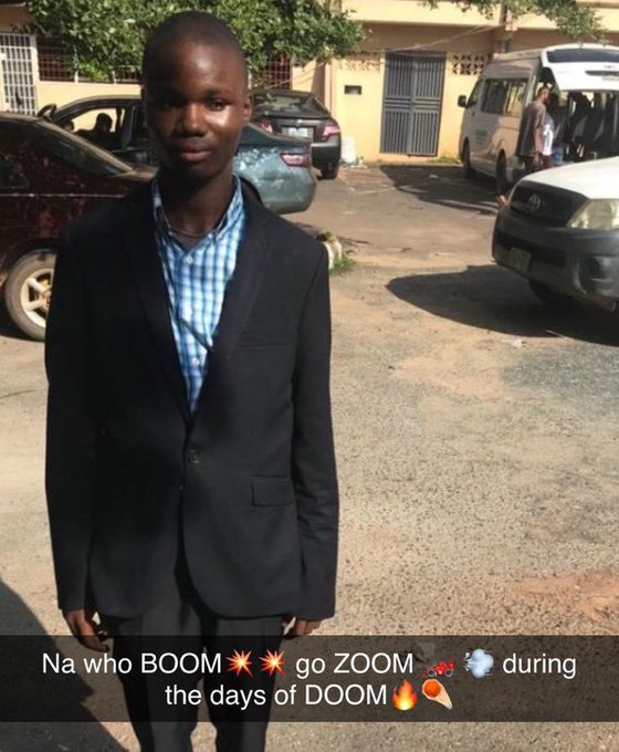 A man in a black suit and blue checkered shirt standing outdoors in a parking lot, with text overlaid reading 'Na who BOOM💥💥 go ZOOM 💨💨☁️ during the days of DOOM🔥🍦'.