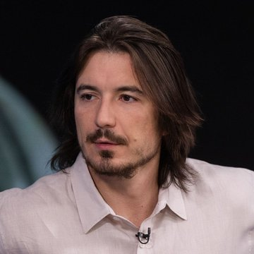 A man with long dark hair and a goatee, wearing a light pink button-up shirt with a lapel microphone, appears to be speaking at an event or interview. Given the post about Robinhood Chain's $42.58 million ETH revenue, the image likely depicts a representative or executive discussing Robinhood's crypto-related financial performance.