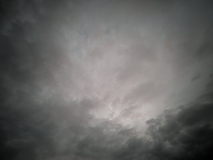 A dramatic view of a dark, cloudy sky with a bright patch of light breaking through the overcast clouds.