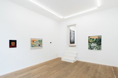 An interior view of a minimalist white art gallery with wooden floors, displaying several framed paintings and a sculpture in a recessed alcove.