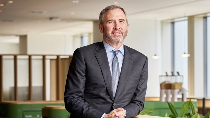 A confident businessman in a dark suit smiles in a modern office setting, visually paired with the post's bullish call to "Buy $XRP now, thank me later." The polished corporate backdrop lends an air of professional credibility to the cryptocurrency investment recommendation.
