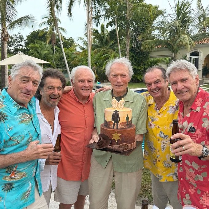 A group of six older men in colorful tropical Hawaiian shirts gather together at a poolside celebration, with one man holding a two-tiered birthday cake featuring "96" and a cowboy figure. Several men hold beer bottles as they smile for the camera, complementing the post's celebratory tone about Bitcoin's projected future value.