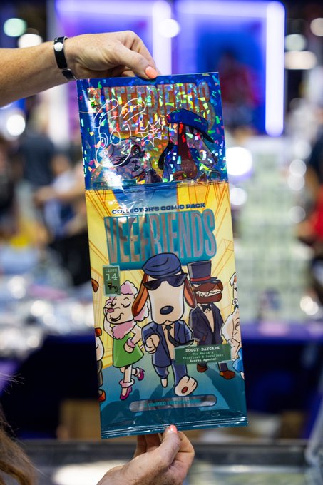 A person holds up a sealed "Idle Hands Collect Hive Comic Pack #14" featuring the "Cracked Ice Doggy Daycare" comic pack at what appears to be a comic convention, with the illustrated cover showing a dog in sunglasses and a top-hatted character matching the "Doggy Daycare" theme referenced in the pull.