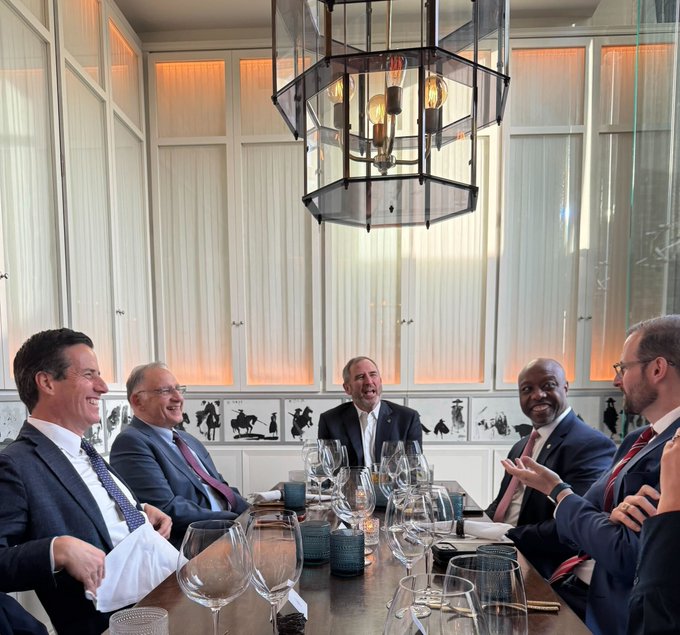 A group of well-dressed businessmen share a laugh at an upscale restaurant beneath an ornate chandelier, suggesting a celebratory gathering. The caption "They can delay XRP, but they can't stop it" implies these men may be financial or crypto executives confidently anticipating the cryptocurrency's inevitable progress despite regulatory pushback.
