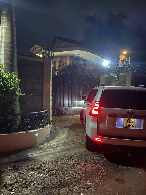 A nighttime photo of a silver Toyota Land Cruiser with license plate 'KDS 006S' parked outside a gated property topped with razor wire.