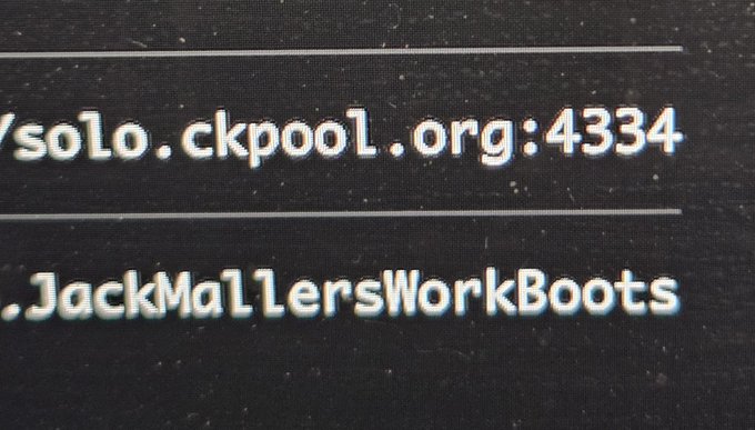 A close-up of a computer screen displays text reading '/solo.ckpool.org:4334' and 'JackMallersWorkBoots' on a black background.
