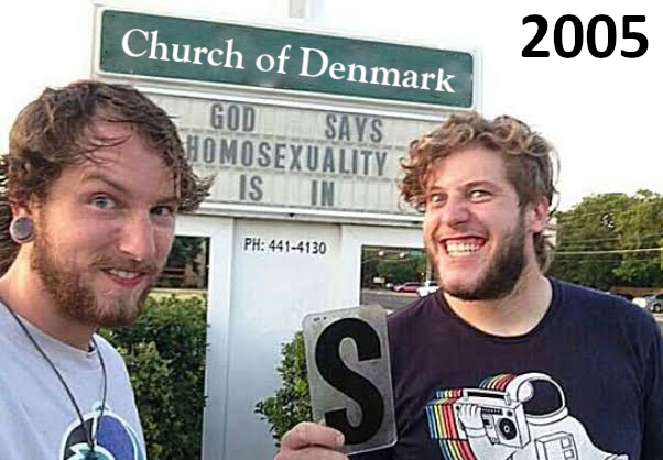 A 2005 photo of two men smiling in front of a 'Church of Denmark' sign with a marquee reading 'GOD SAYS HOMOSEXUALITY IS [SIN]'; one man holds up a black letter 'S' to complete the sign's message.
