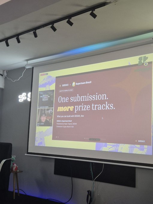A presentation slide projected onto a screen reads 'One submission. more prize tracks.' for a SODAX x Superteam Brazil crypto hackathon.