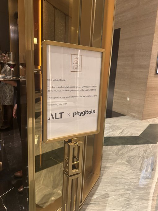 A framed sign in a lobby announcing 'ALT × phygitals', stating that a bar is exclusively booked for an ALT VIP Reception from 21:00 to 24:00 and cannot accommodate walk-in guests.
