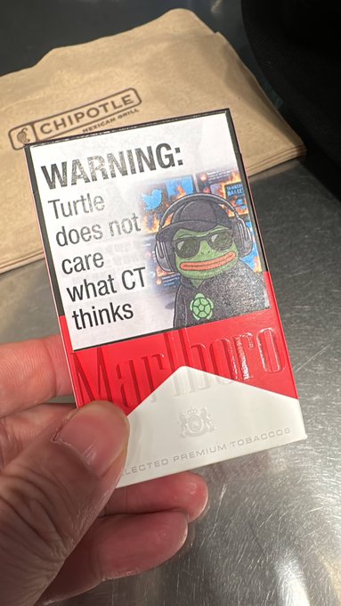 A hand holds a red Marlboro cigarette pack featuring a 'WARNING: Turtle does not care what CT thinks' label with a cartoon turtle wearing sunglasses and headphones, placed in front of a Chipotle paper bag.