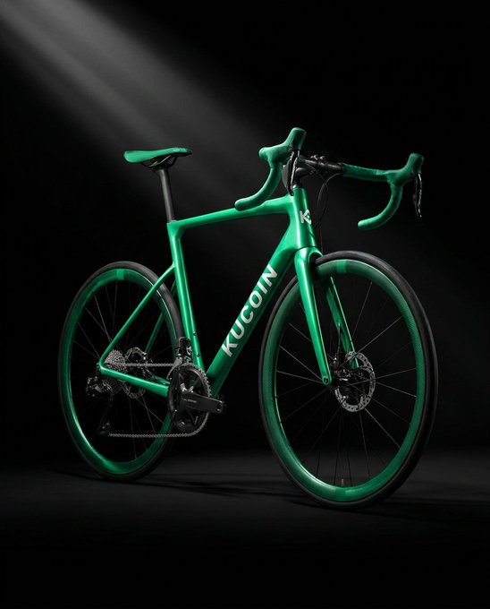 A sleek green road bike branded with "KuCoin" is dramatically lit against a dark background, perfectly suited to the caption's theme of tackling legendary climbs with a single, capable machine.