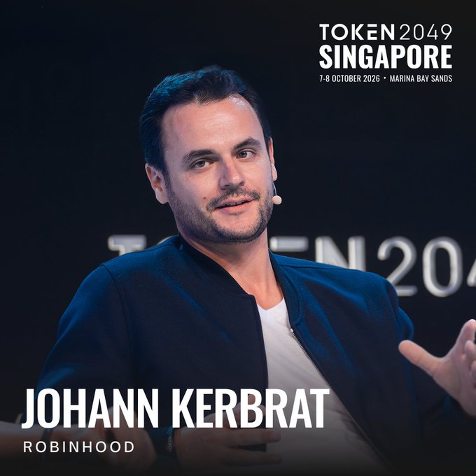 A man in an orange "ETHGLOBAL" shirt speaks on stage at TOKEN2049 Singapore (7-8 October 2026, Marina Bay Sands), identified as Johann Kerbrat of Robinhood, pictured here as one of the Ethereum figures the post playfully suggests should "fight."