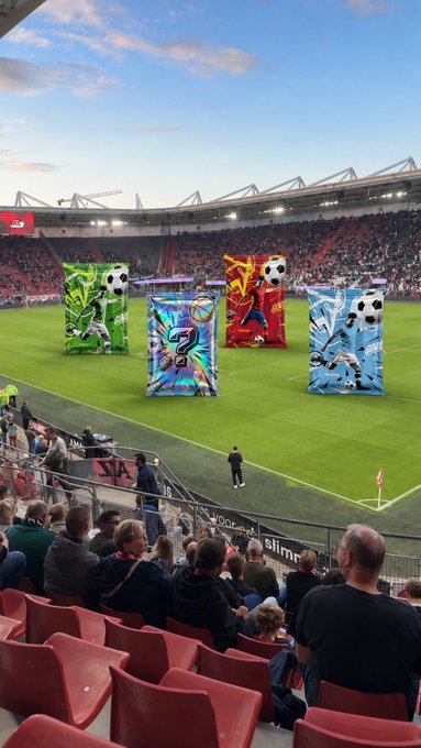 Colorful graffiti-style inflatable sculptures featuring soccer balls stand on the pitch at what appears to be a stadium event, likely related to a sports NFT pack promotion on Rarible. The image ties directly to the post by showcasing the variety of unique sports-themed digital art designs ("slabs") available in their collection, encouraging viewers to pick their favorites.