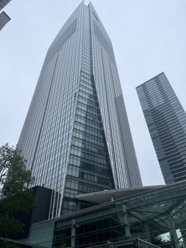 A low-angle view captures a tall modern glass skyscraper reaching into an overcast sky alongside neighboring high-rises.