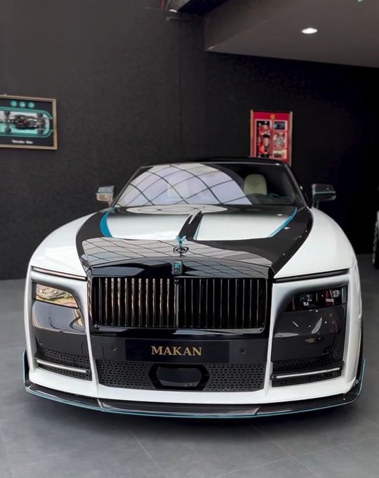 The image features a luxury car, specifically a Rolls Royce, parked inside a showroom with black walls. The car has a sleek design and is positioned prominently in front of a mirror. The caption provided by the image suggests that the system watching the car's actions might be learning how to drive or perform certain maneuvers, but it could also be observing other aspects of driving behavior such as speed, handling, or style preferences.