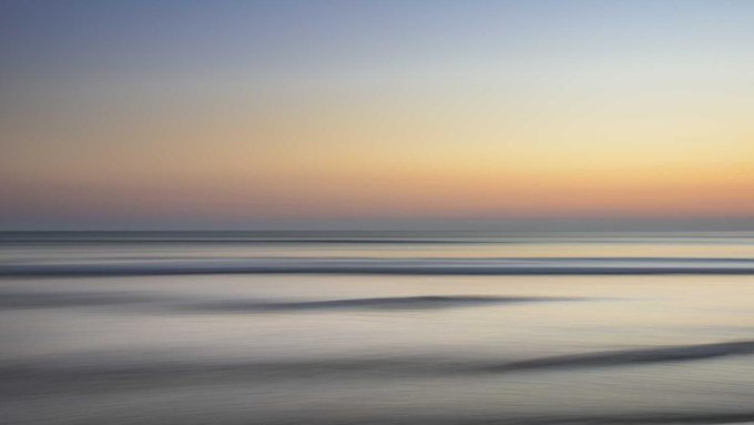 The image shows an ocean scene with a beautiful sunset over the water, creating a serene atmosphere. The sun is setting behind the horizon, casting a warm glow across the sky. The ocean has gentle waves that are rippling outwards from the center of the frame. In the background, there's a post about Bitcoin and cryptocurrency, which seems to be discussing the current state of the market. The post highlights how ADA and HYPE have been holding up while Bitcoin struggles for direction.