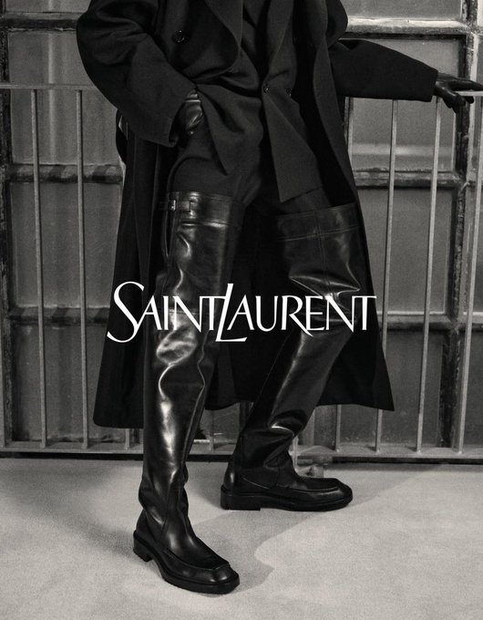A black and white Saint Laurent fashion campaign image featuring a model in an oversized coat and thigh-high leather boots, with the 'SAINT LAURENT' logo overlaid.