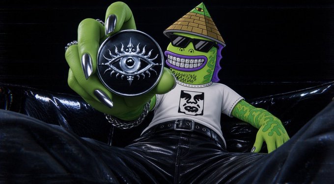 A green-skinned cartoon character wearing a pyramid hat and sunglasses holds up a black medallion featuring an all-seeing eye, lounging in a black leather chair while wearing a white t-shirt with a stylized face logo. The mystical, "all-seeing eye" imagery complements the post's cryptic, conspiratorial tone about locked-in phases and exclusive subscriber access.