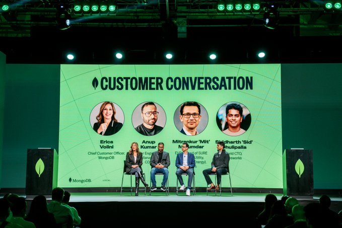 A conference stage photo from MongoDB featuring a 'Customer Conversation' panel with four speakers (Erica Volini, Anup Kumarar, Mitrankur 'Mit' Mukherjee, and Siddharth 'Sid' Mulugalle) seated in front of a green backdrop with their photos displayed.