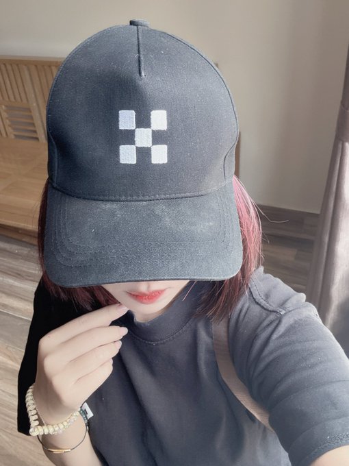 Photo of a woman with pink-streaked hair wearing a black Under Armour cap with the brand's logo, taking a selfie with her hand near her face.