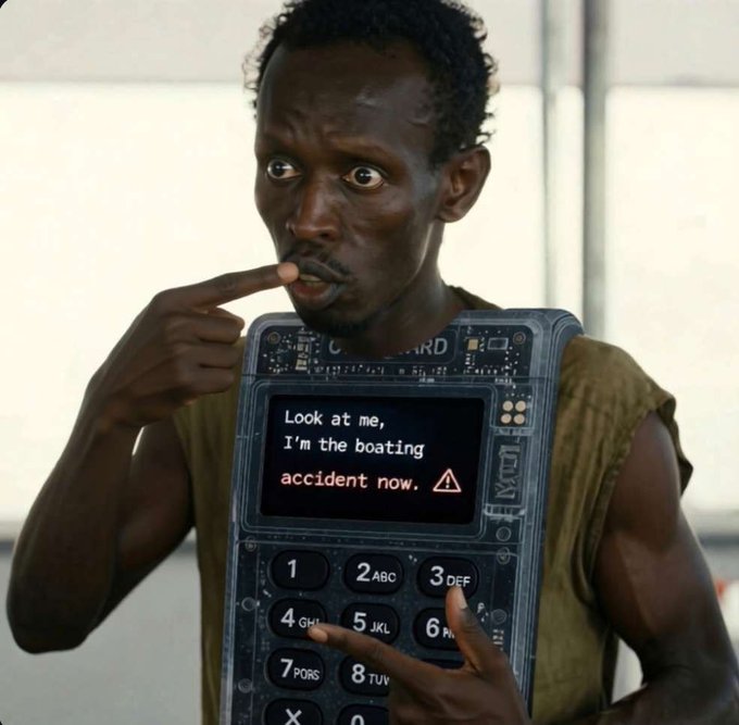 A man wearing a costume that resembles a large feature phone with a screen displaying the text "Look at me, I'm the boating accident now." alongside a warning emoji, appearing to be from a comedy skit.