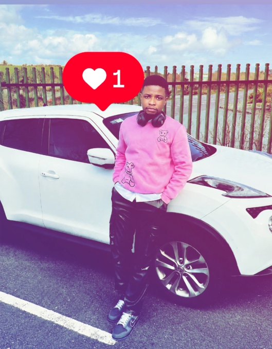 A young boy wearing a pink sweatshirt and black pants stands in front of a white car, with a red heart notification graphic showing '1' like.