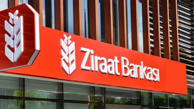 A bright red sign displays "Ziraat Bankası" with its wheat-sheaf logo outside a modern building, representing the Turkish state bank where the user recently transferred their accounts. The image ties directly to the post's mention of moving financial assets to Ziraat, while the wheat emblem serves as a subtle nod to the sports-related "Fenerbahçe" reference, given Fenerbahçe's nickname and branding similarities.