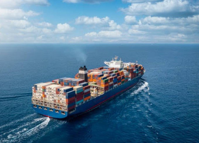 Aerial view of a large blue container ship loaded with colorful shipping containers sailing across the open ocean.