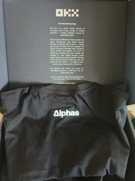 A person displays a black OKX-branded hoodie and jersey inside a sleek black box, with the OKX logo and an inspirational message visible on the inner lid. The post expresses excitement about receiving the merchandise from OKX's World Cup prediction event, praising the quality and design of the Erling Haaland–style jersey.