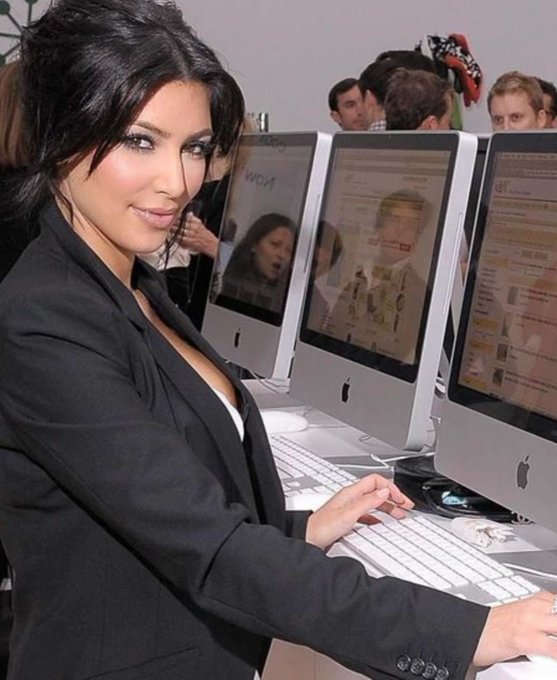 Kim Kardashian posing in front of Apple iMac computers at what appears to be a promotional or media event.